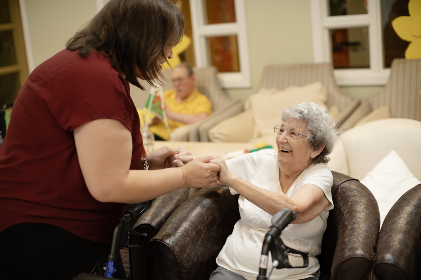 Pflegekraft hilft einer lachenden Seniorin beim Aufstehen